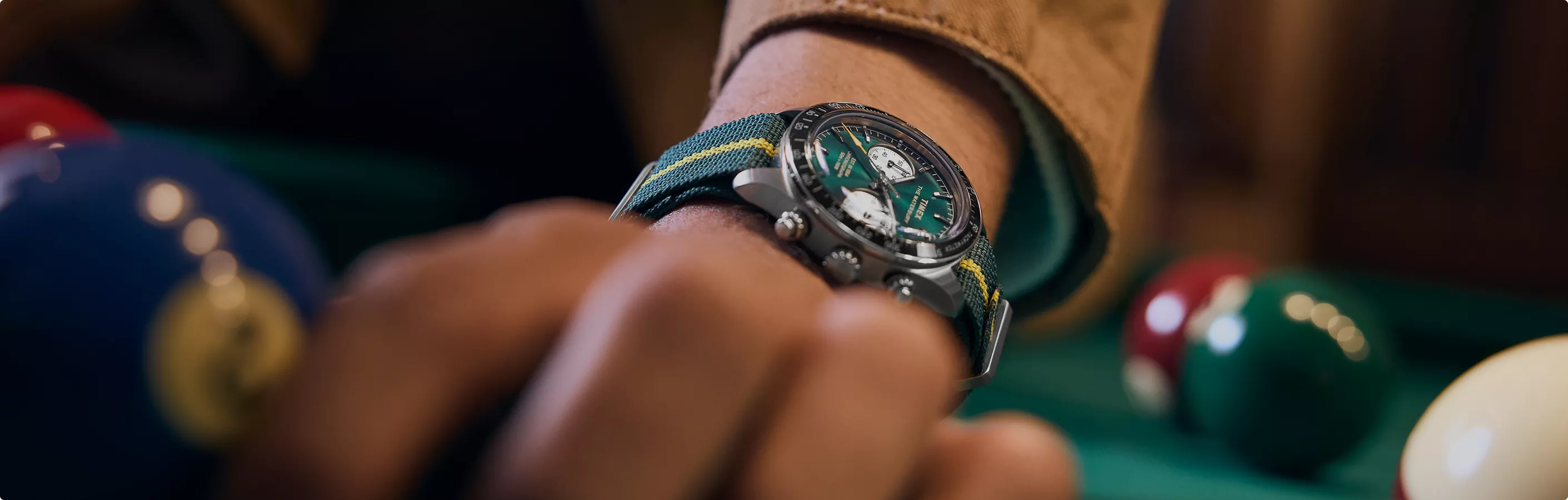 Luxuriöse Armbanduhr mit grünem Zifferblatt am Arm eines Mannes beim Billardspielen